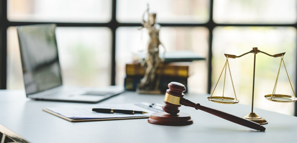 law firm courtroom Law books, computer and scales of justice on table in lawyer office